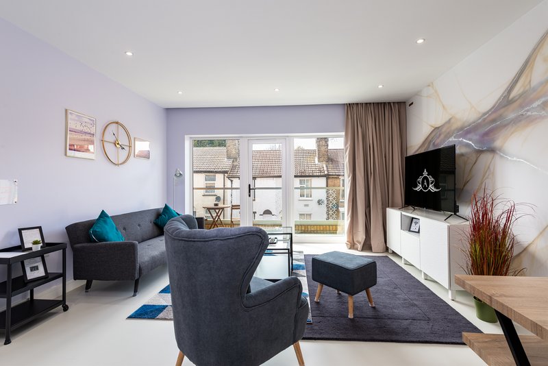 Modern living room with grey sofa, armchair, TV, and patio doors overlooking garden