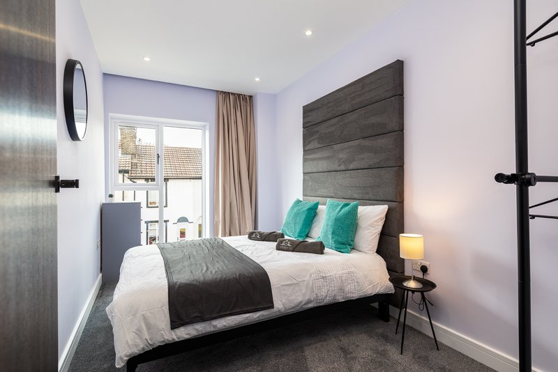 Modern bedroom with double bed, dark headboard, green cushions, bedside table and window