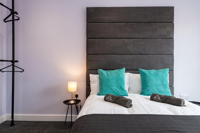 Modern bedroom with grey upholstered headboard, turquoise pillows, white bedding and bedside lamp