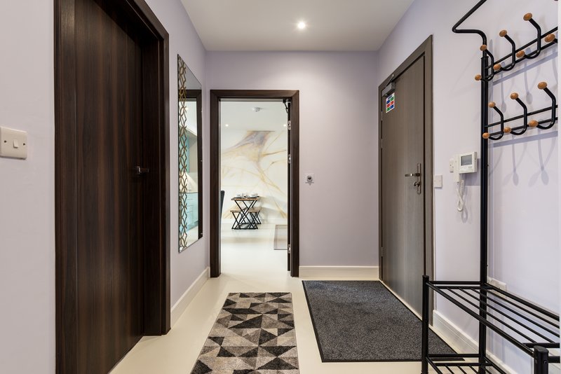 Modern hallway with dark wooden doors, patterned floor mat, and wall-mounted coat rack
