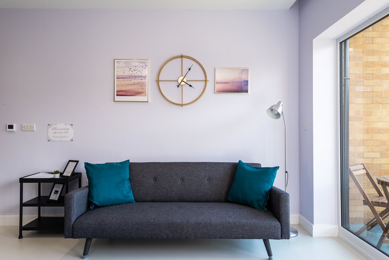 Modern living room with dark grey sofa, teal cushions, wall art and clock