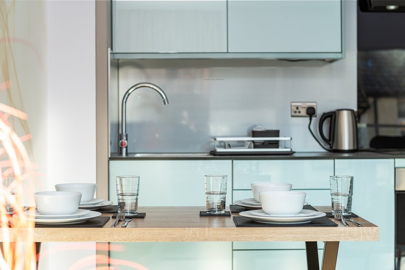 Modern kitchen with light blue cabinetry, wooden countertop, place settings and kettle