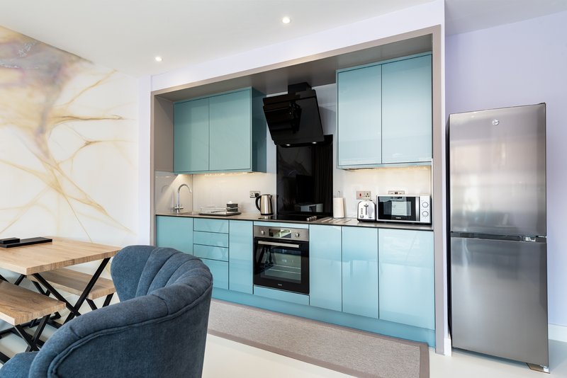 Modern kitchen with turquoise cabinetry, stainless steel appliances, and adjacent seating area