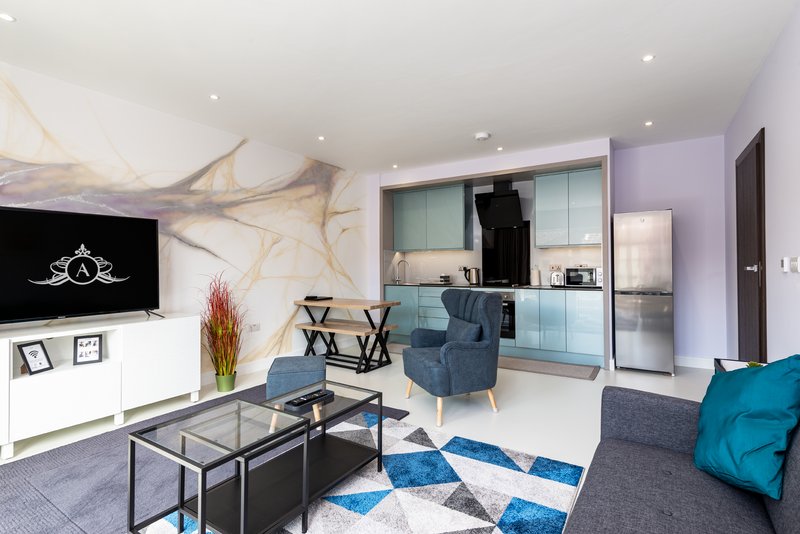 Modern open-plan living room with kitchen, TV, sofa, and blue geometric rug