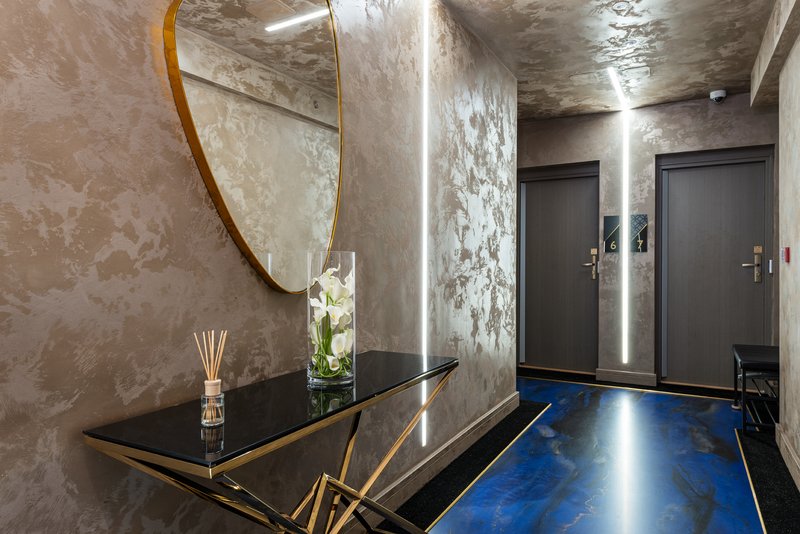Modern hallway with polished blue concrete floor, console table, round mirror and dark doors