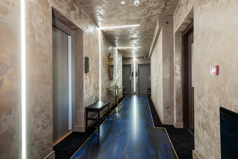 Modern hallway with polished concrete floor, marble walls, linear ceiling lights and multiple doors