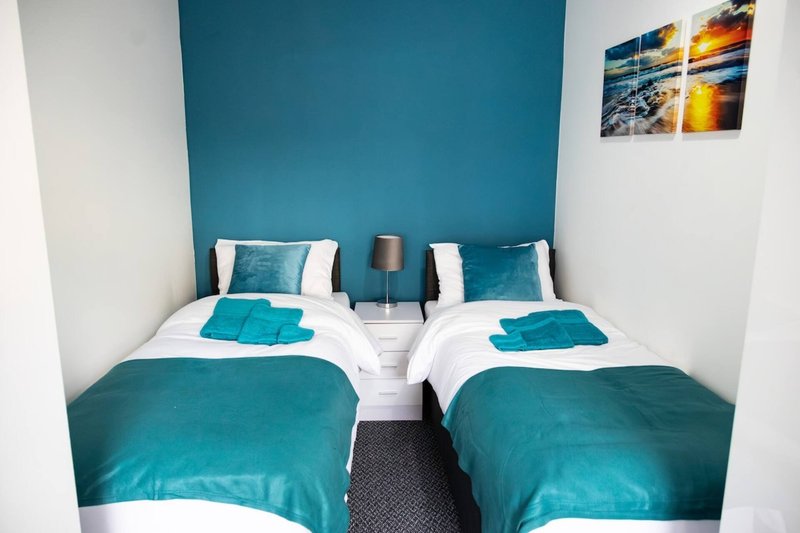 Twin bedroom with teal feature wall, white bedding, matching cushions and throws