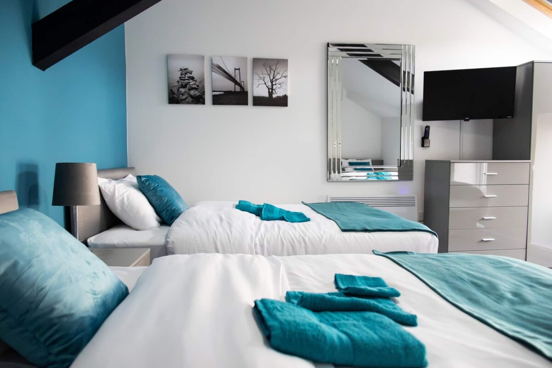 Modern bedroom with twin beds, turquoise accents, wall art, and mirrored wardrobe