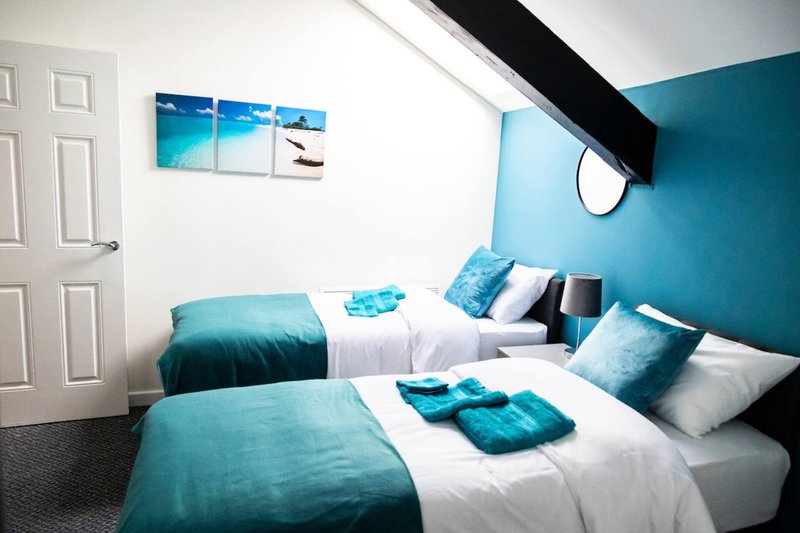 Twin bedroom with turquoise accent wall, white bedding, blue cushions and beach-themed wall art