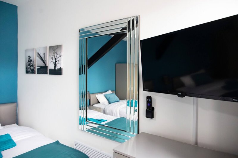 Modern bedroom with turquoise accents, mirrored wardrobe, wall-mounted TV, and white bedding