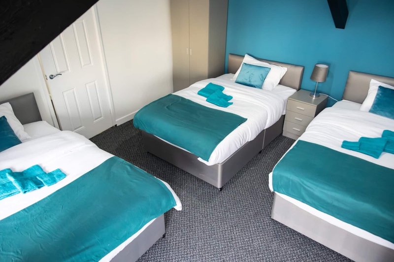 Bright bedroom with three single beds, teal bedding, white pillows, and blue accent wall