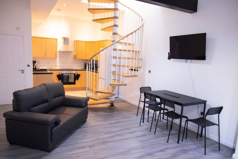 Open-plan living area with black sofa, dining table, spiral staircase and kitchen