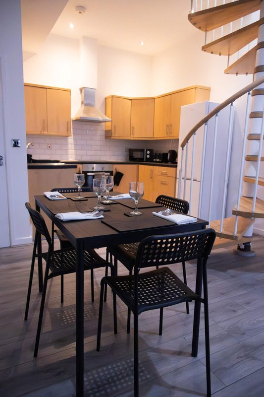 Open-plan kitchen and dining area with wooden cabinets, black dining table, stairs visible