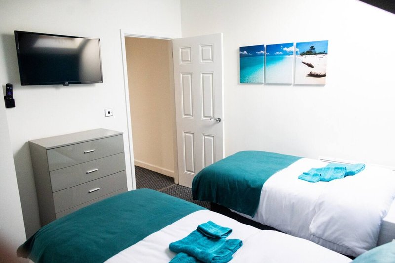 Bright bedroom with two single beds, grey dresser, wall-mounted TV and beach-themed wall art