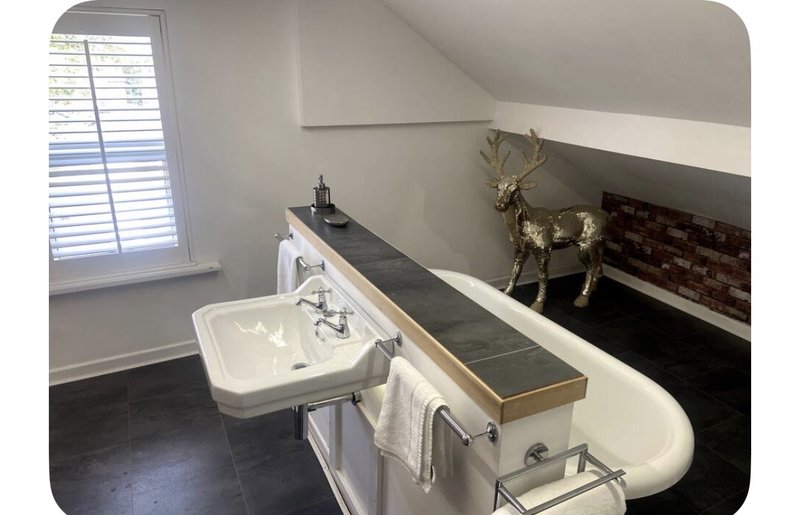 Attic bathroom with pedestal sink, freestanding bathtub, window, and decorative deer statue