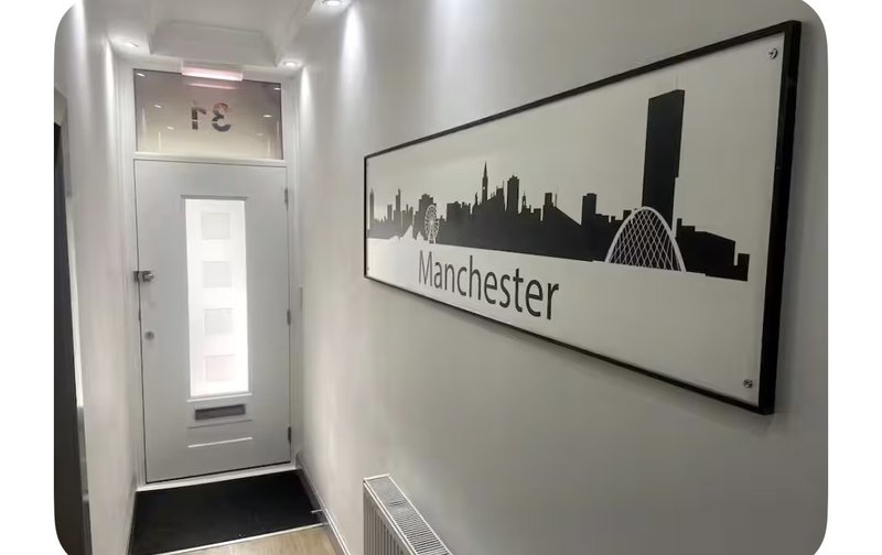 Narrow hallway with white walls, entrance door, and Manchester skyline wall art