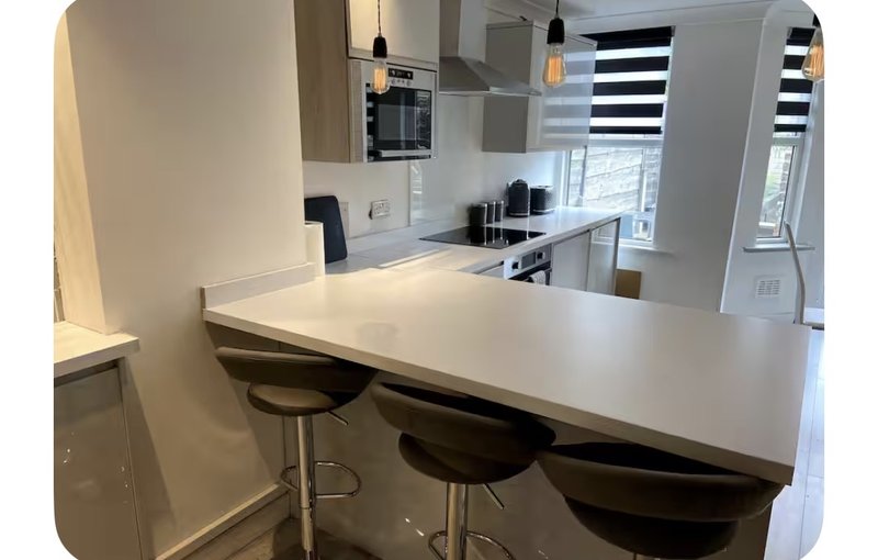 Modern kitchen with white countertop, bar seating, built-in oven, and striped window blinds
