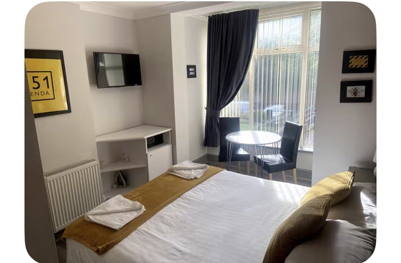 Bright bedroom with double bed, desk, wall-mounted TV, and access to balcony with seating area