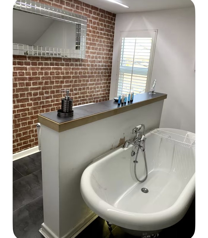 Modern bathroom with exposed brick wall, pedestal sink, freestanding bathtub and mirror shelving