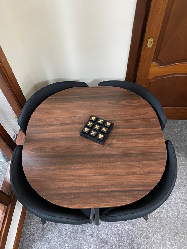 Overhead view of wooden dining table with black chairs and board game