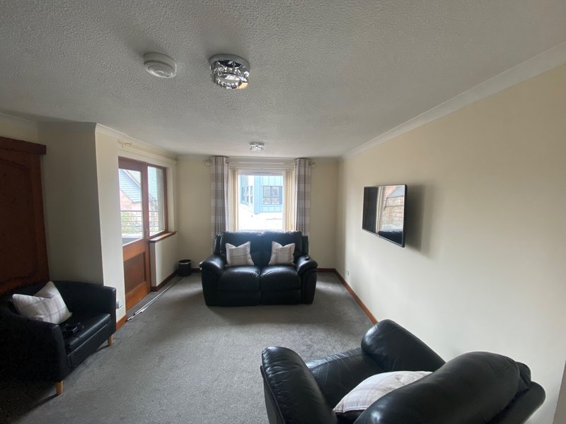Living room with black leather sofas, windows with curtains, cream walls and carpet flooring