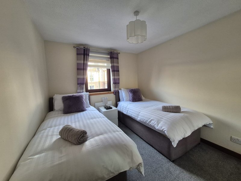Twin bedroom with two single beds, purple curtains, pendant light and window