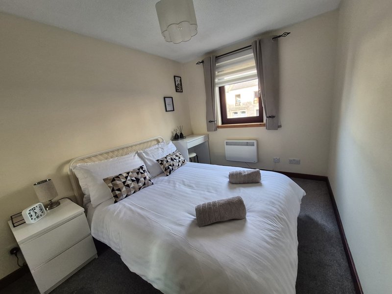 Bedroom with double bed, white bedding, patterned pillows, window with blinds and radiator