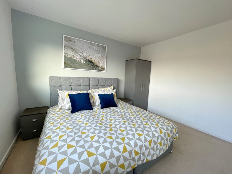 Modern bedroom with double bed, geometric patterned duvet, blue cushions and grey headboard