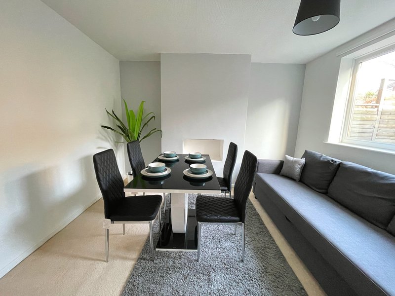 Modern dining area with black table, four chairs, place settings, and gray sofa beside window