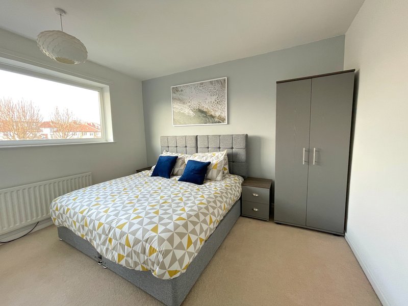 Modern bedroom with double bed, geometric bedding, wardrobe, and window with natural light