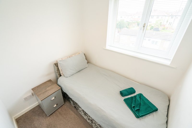 Minimalist bedroom with single bed, pillow, green towel, wooden nightstand and window