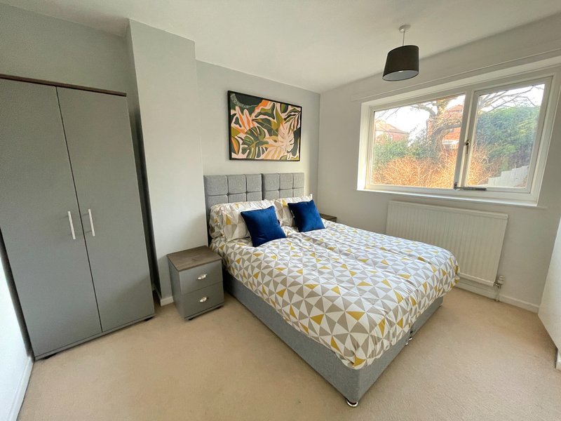 Modern bedroom with double bed, geometric bedding, wardrobe, and large window with autumn views
