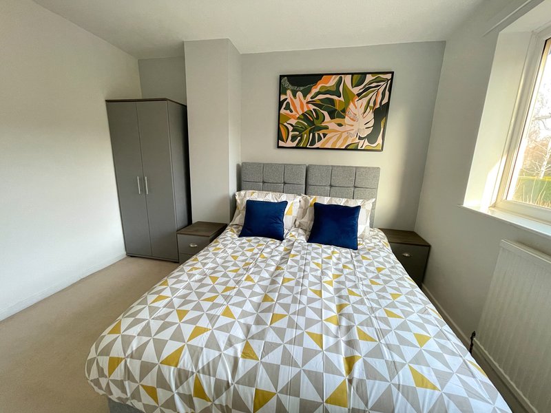 Modern bedroom with double bed, patterned duvet, blue pillows, grey wardrobe and framed wall art