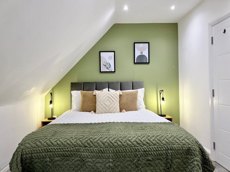 Attic bedroom with double bed, green accent wall, framed artwork, and bedside lighting