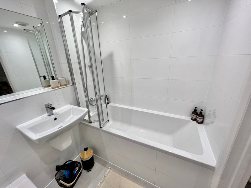 Clean modern bathroom with white tiles, sink, mirror, bathtub and shower screen