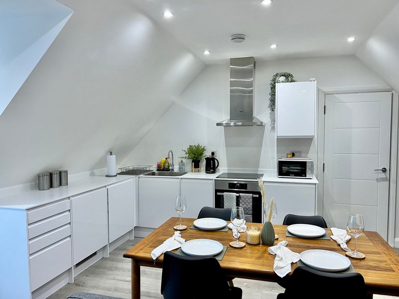 Modern attic kitchen with white cabinetry, dining table set for four, and skylight window