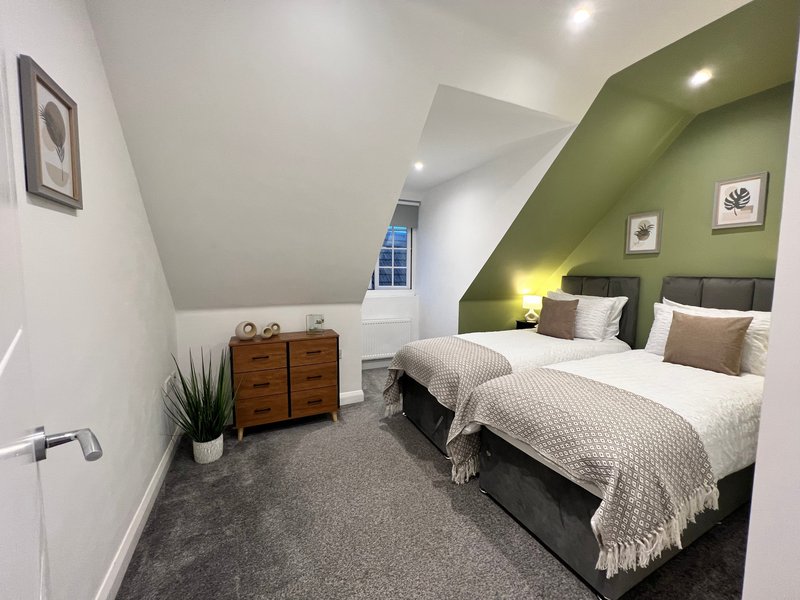 Twin bedroom with olive-green accent wall, two beds, wooden chest of drawers, and skylight window
