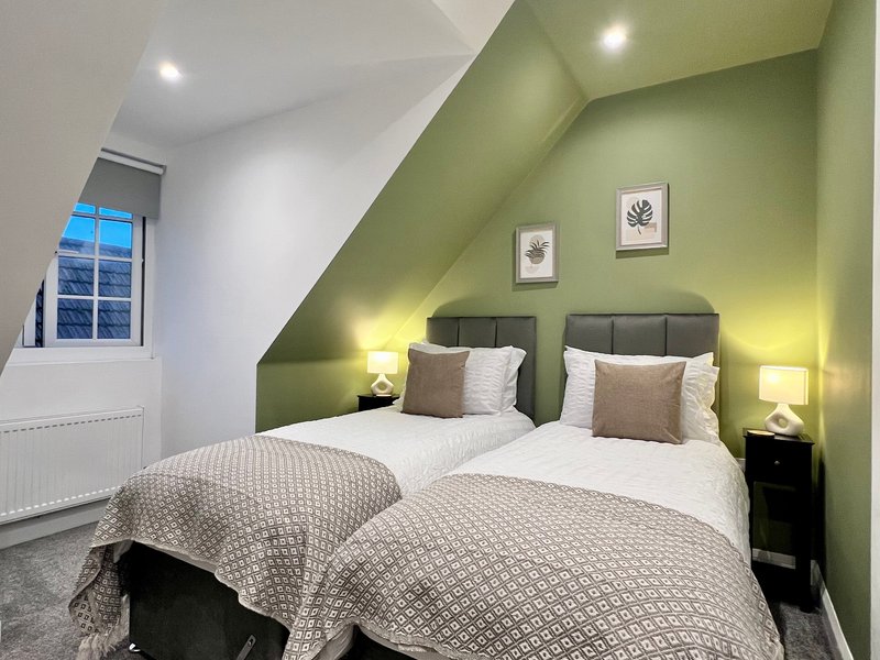 Bedroom with two single beds, green accent wall, window, and bedside lamps