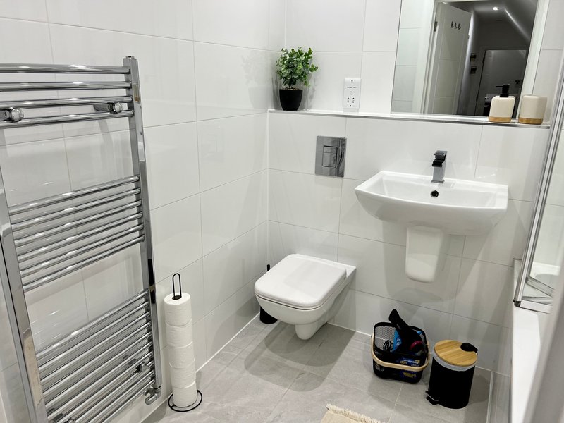 Modern bathroom with white tiles, heated towel rail, pedestal sink, toilet and mirror