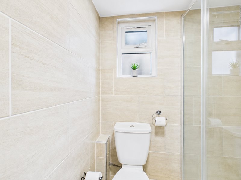 Compact bathroom with toilet, shower enclosure, tiled walls, window and shelf