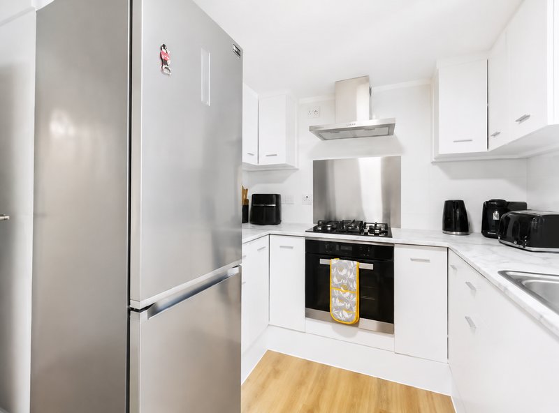 Modern white kitchen with stainless steel fridge, gas hob, and wooden flooring