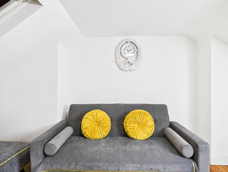 Gray upholstered sofa with yellow round cushions and wall clock above