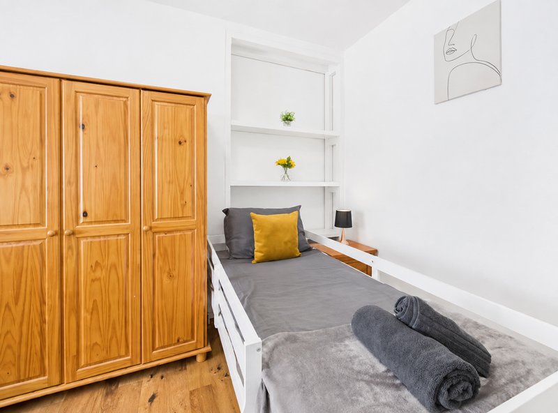 Bedroom with wooden wardrobe, single bed with gray bedding, yellow pillow, and wall shelving
