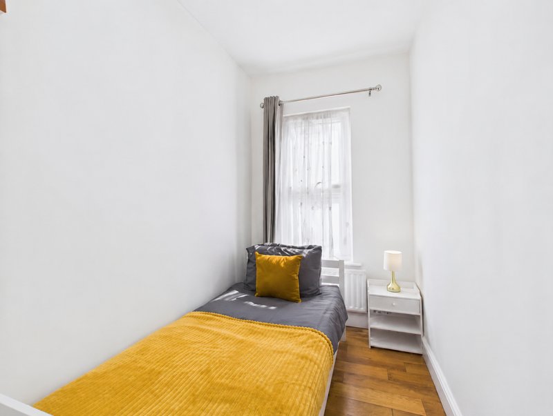 Bright single bedroom with yellow bedding, gray cushion, window with curtains and wooden floor