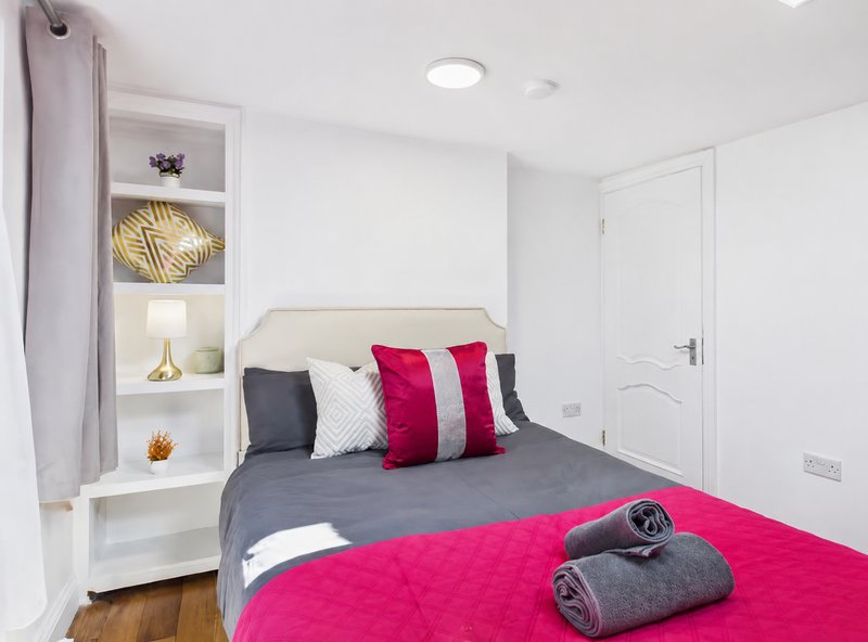 Modern bedroom with double bed, grey and pink bedding, white shelving unit and recessed lighting