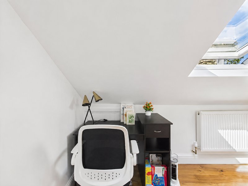 Bright attic bedroom with skylight, white walls, wooden floor, and compact storage shelving