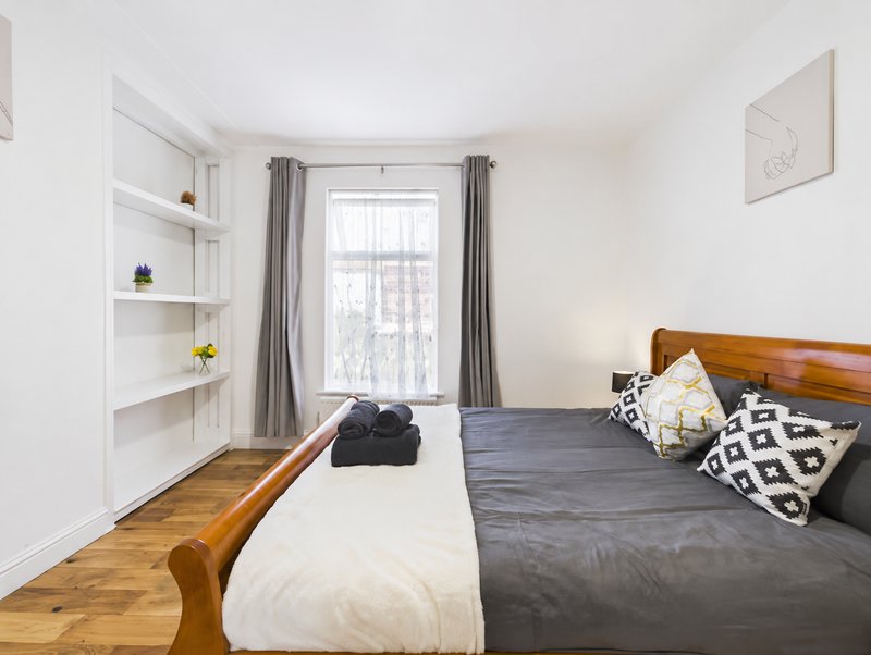 Bright bedroom with wooden bed frame, grey curtains, shelving, and hardwood flooring