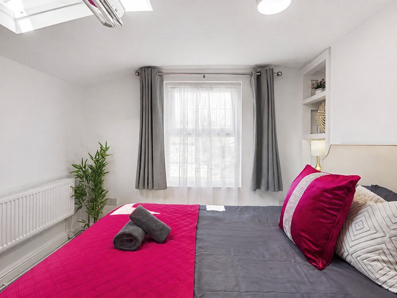 Bright bedroom with double bed, pink bedding, grey curtains and potted plant