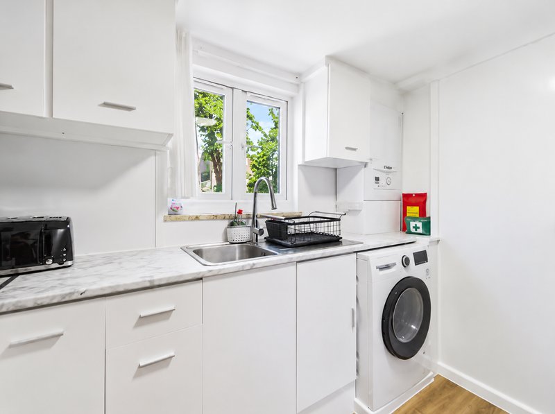 Modern white kitchen with marble countertop, sink, appliances, washing machine and garden view