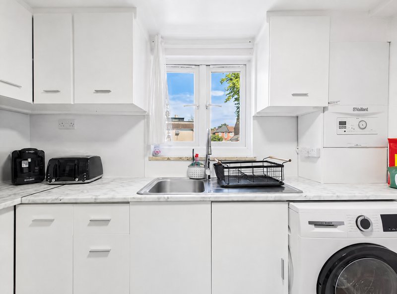 Modern white kitchen with sink, appliances, and view through window to garden